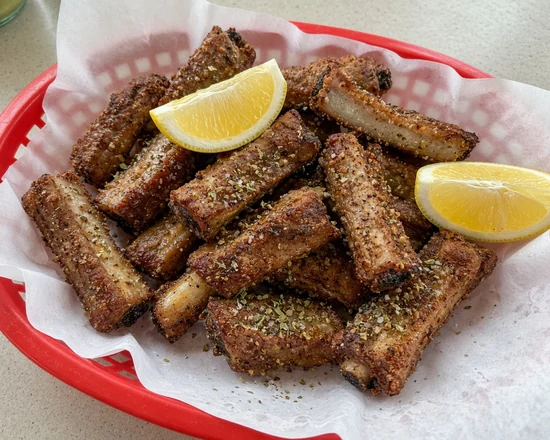 Basket of crispy Greek dry ribs with oregano and lemon wedges