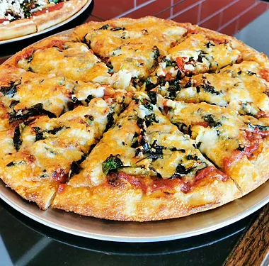 Spinach and cheese pizza cut into slices on a pizza pan at the Nitza's counter